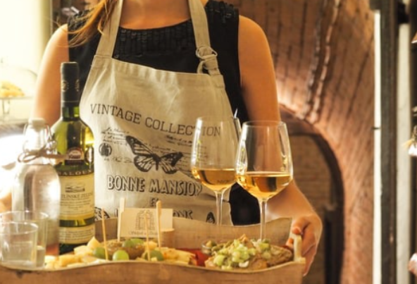 Smiling hostess at a wine distillery carrying a charcuterie board and fine wines for Culture Calendar women’s social group experience in Merseyside