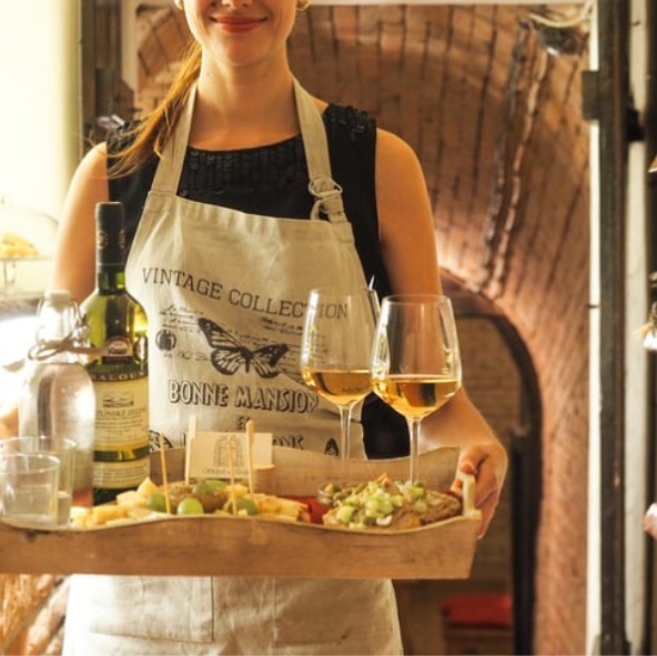 Smiling hostess at a wine distillery carrying a charcuterie board and fine wines for Culture Calendar women’s social group experience in Merseyside