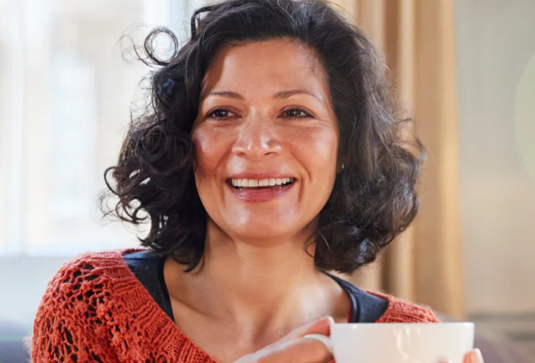 Smiling woman sitting alone with a cup of tea, excited to join a local women’s social group in Merseyside and West Lancashire that explores arts, culture, and nationwide events.