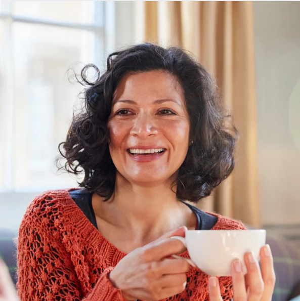 Smiling woman sitting alone with a cup of tea, excited to join a local women’s social group in Merseyside and West Lancashire that explores arts, culture, and nationwide events.