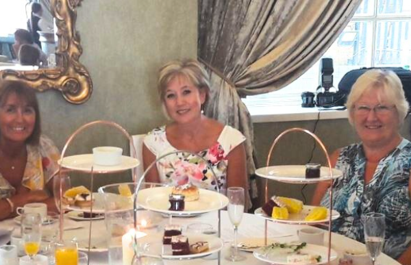 Elegantly dressed women seated at a round table, enjoying champagne and laughter during a glamorous Murder Mystery Afternoon Tea with Culture Calendar Women’s Social Group in Merseyside and West Lancashire.