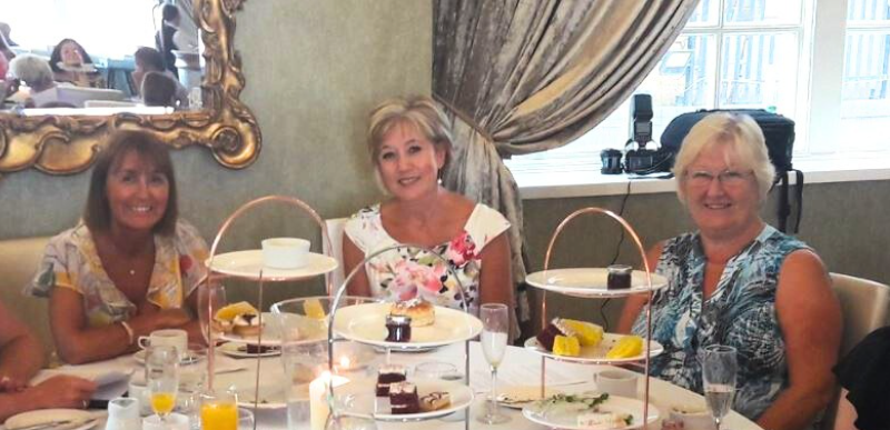 Elegantly dressed women seated at a round table, enjoying champagne and laughter during a glamorous Murder Mystery Afternoon Tea with Culture Calendar Women’s Social Group in Merseyside and West Lancashire.